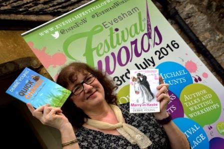 Photo Of Debbie Holding Up Two Of Her Books In Front Of A Festival Banner