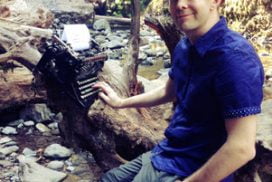 Derek Murphy outdoors by a waterfall with a typewriter