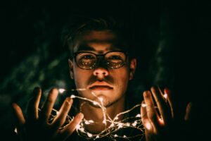Photo of bespectacled man holding mysterious string of lights in the dark