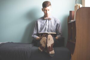 photo of man reading with book on lap, legs stretched out, showing soles of shoes