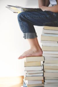 photo of person sitting on pile of books reading one