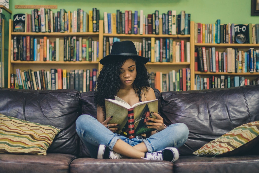 photo of girl sitting on sofa reading book in front of extensive bookshelves to illustrate what makes readers buy books