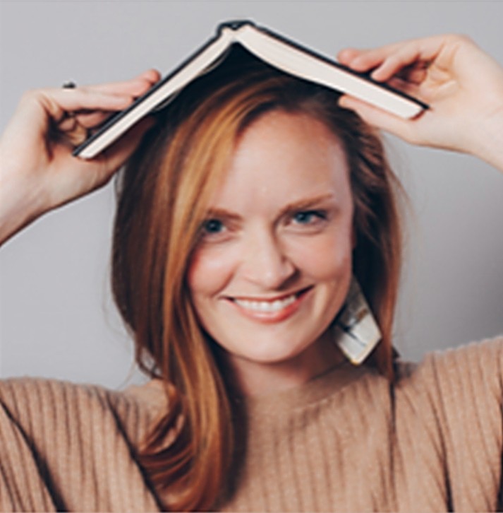 Headshot Of Meghan Harvey With Book On Her Head
