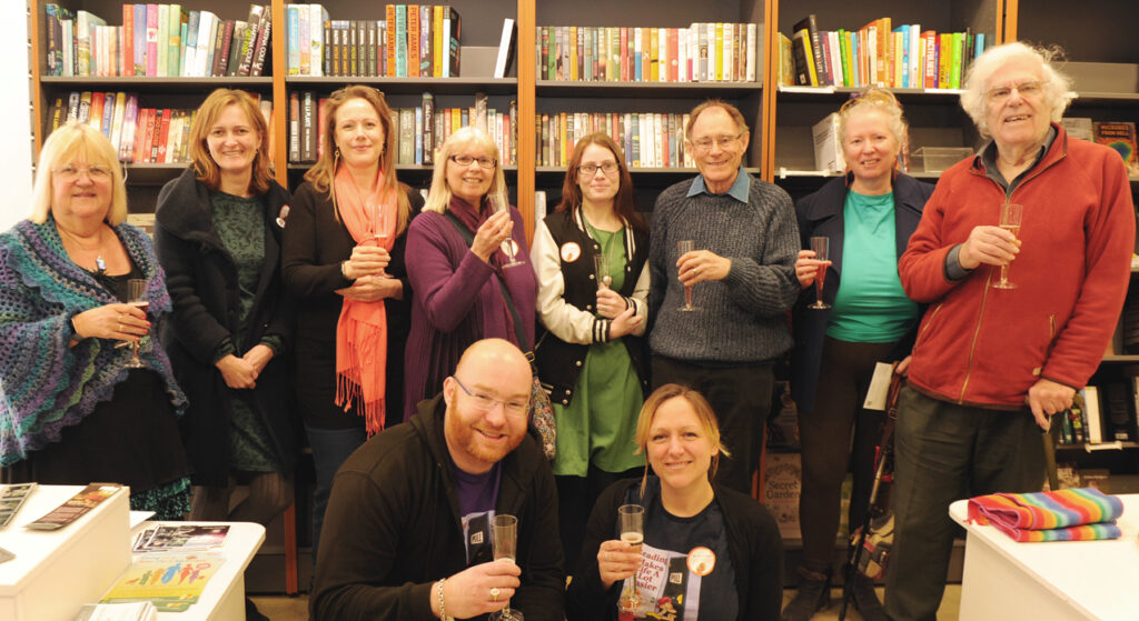 photo of them with glass of bubbly in front of bookshelves