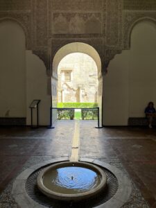 Real Alcazar palace, room with internal circular fountain with water ditch in the tiles that leads outside through an arched open door into a courtyard